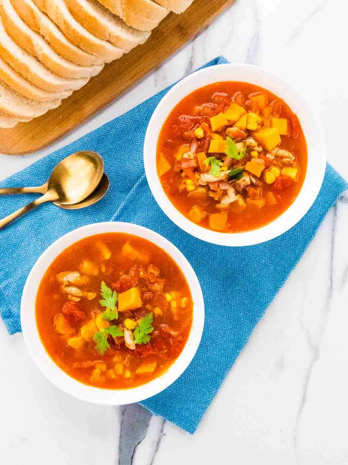 2 bowls full of healthy chicken and chorizo soup with sliced bread