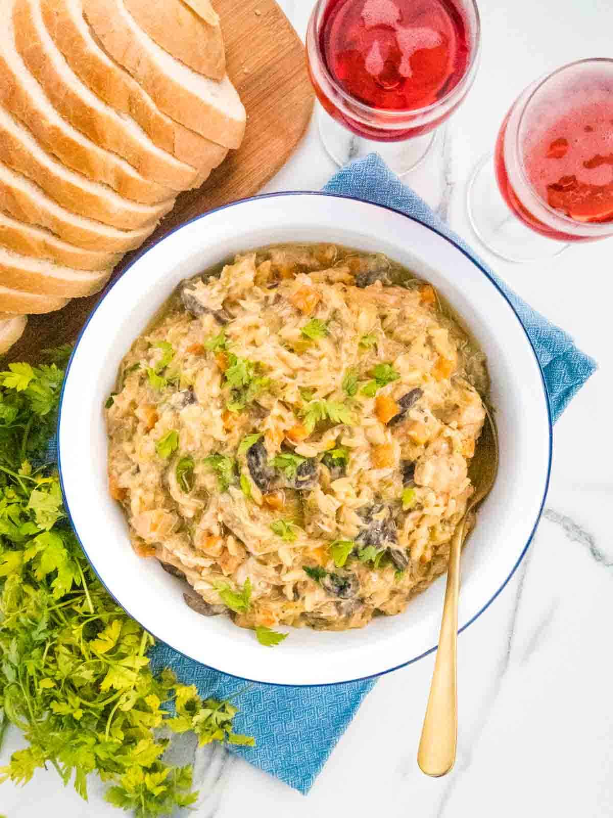 large enamel dish full of creamy orzo risotto served with bread, wine and parsley