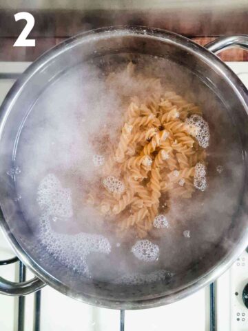 person boiling wholewheat fusilli pasta in a large pan of salted water