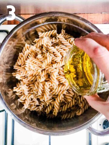 person drizzling extra virgin olive oil into cooked and drained al dente pasta