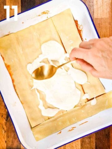 pasta sheets on top of beef bolognese and person spreading a layer of bechamel sauce on top with the back of a spoon