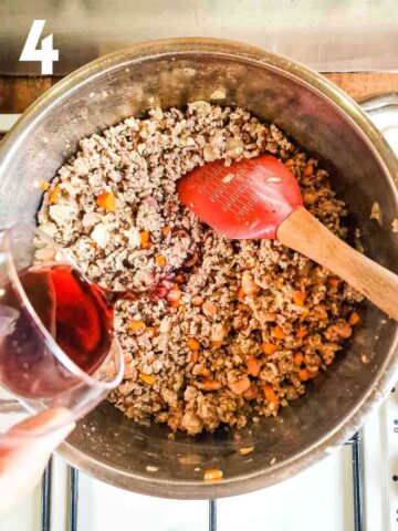 person pouring a glass of red wine into cooked minced beef and pork to make a lasagne bolognese
