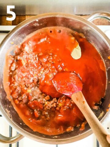 person stirring passata, tomato puree, celery and bay leaf into a red sauce for lasagne