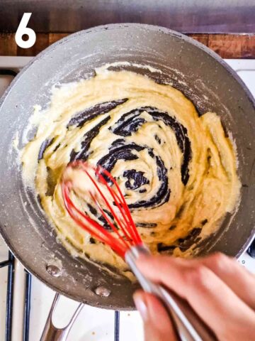 person cooking flour and butter to make a bechamel sauce roux in frying pan with whisk