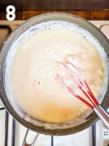 person stirring lasagne creamy white sauce while bubbling and thickening in large pan on hob