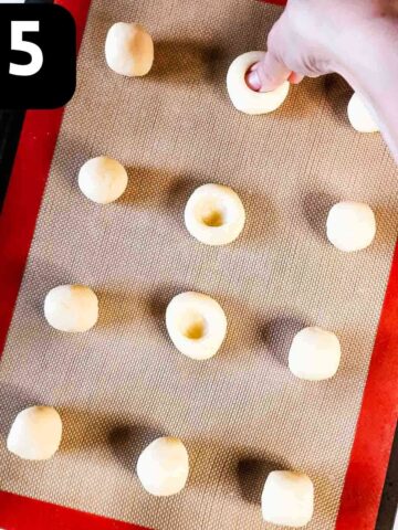 person pressing holes in the centre of cookies dough balls with their thumb