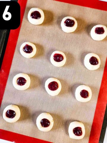 jam filled in cookie dough balls on a silicone baking mat on baking sheet