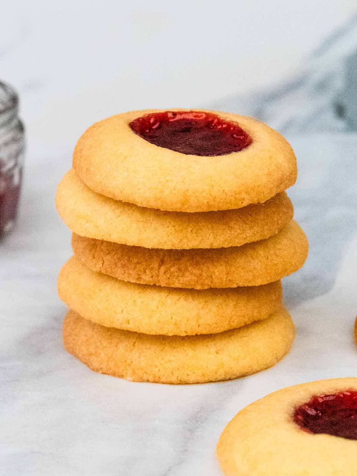 close up of a stack of shortbread thumb print cookies with raspberry jam